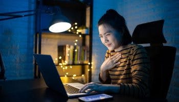 A woman sitting in front of her laptop in the dark while holding her chest.