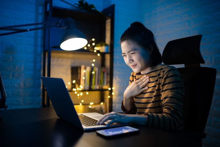 A woman sitting in front of her laptop in the dark while holding her chest.