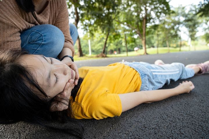 A woman supporting the head and neck of a girl lying unconscious on a pavement