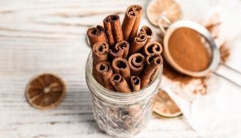 Cinnamon sticks in a small mason jar on a table next to a strainer filled with cinnamon powder