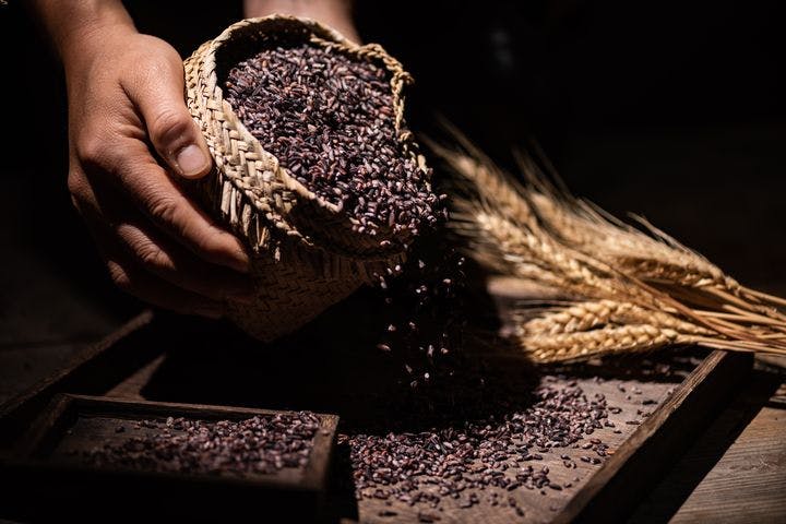 Man pouring black rice from a basket onto a wooden tray