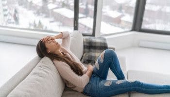 Woman sitting on a sofa in pain while holding her forehead with her left hand 