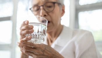 Elderly woman holding a glass of water in her right hand as she supports it using her left