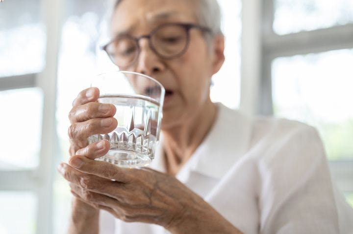 Elderly woman holding a glass of water in her right hand as she supports it using her left
