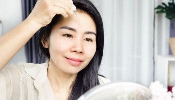 Asian woman applying facial oil using a dropper onto her face