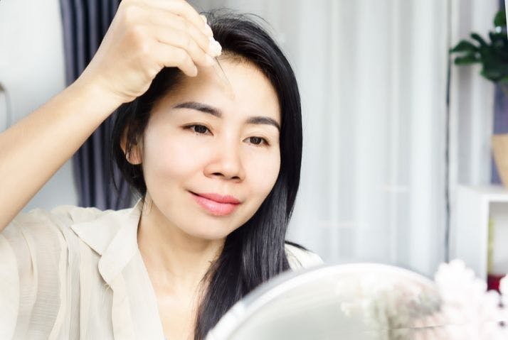 Asian woman applying facial oil using a dropper onto her face