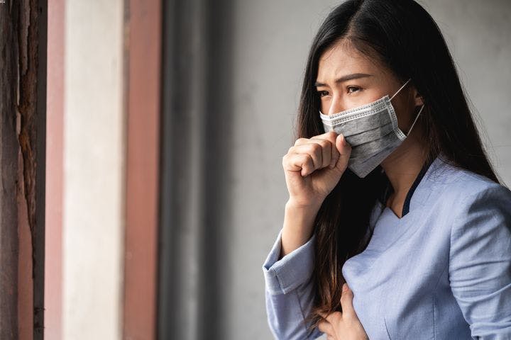 Woman wearing surgical face mask coughing and holding her chest