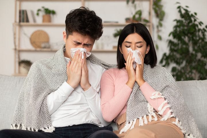 Asian couple having a cold and blowing nose in a paper tissue