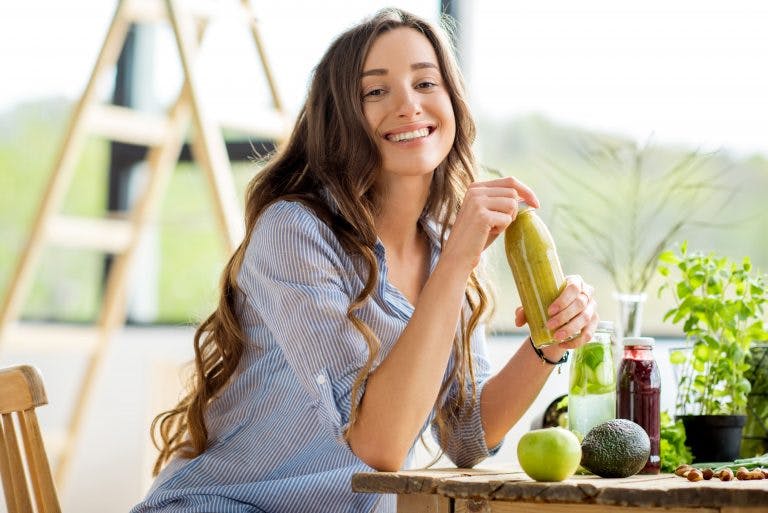 Beautiful happy woman sitting with drinks and healthy green food at home