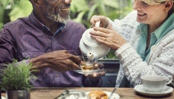A white senior woman pouring tea in a glass for a black senior man