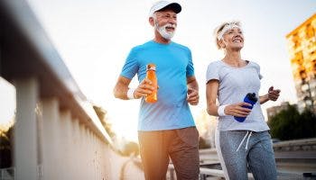 Mature couple jogging and running outdoors in city holding water bottles