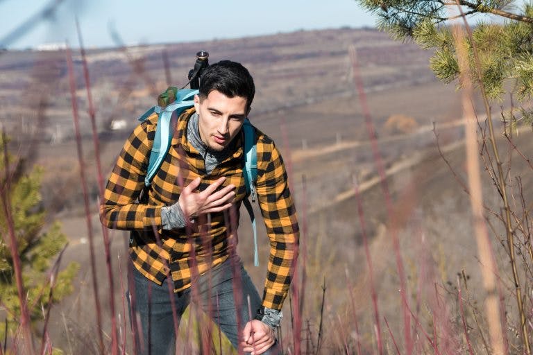 A young man wearing yellow plain shirt having chest pain during a hike