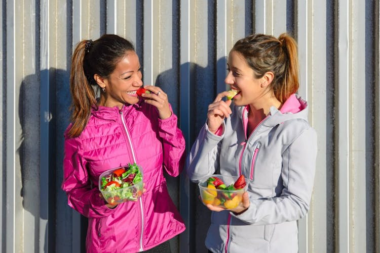 Two women eating salad and fruits on a healthy diet after a workout