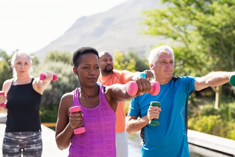 A group of older adults exercising outdoors with dumbbell set