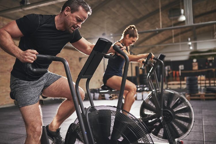 A physically fit man and a woman practicing with air bikes in a gym