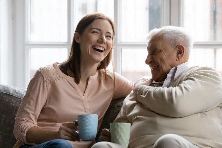 a woman and an old man laughing together while drinking tea