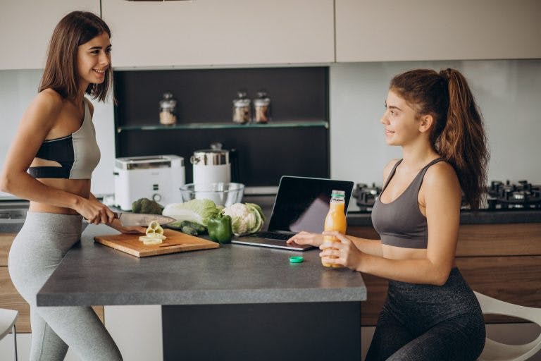 Two women wearing gym clothes preparing meals in the kitchen
