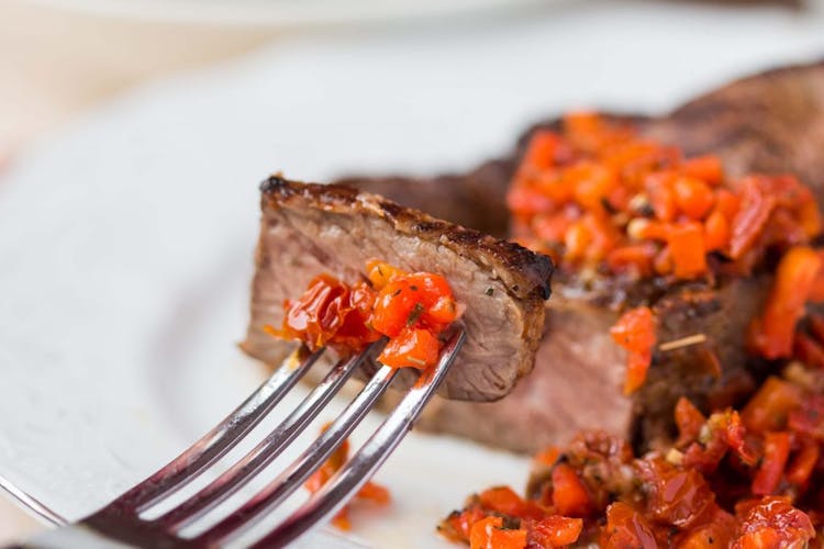 A well-done, well cooked beef steak with forks and salsa