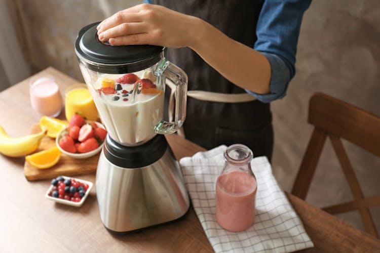 A person mixing yogurt with fresh fruits on a blender to make a smoothie