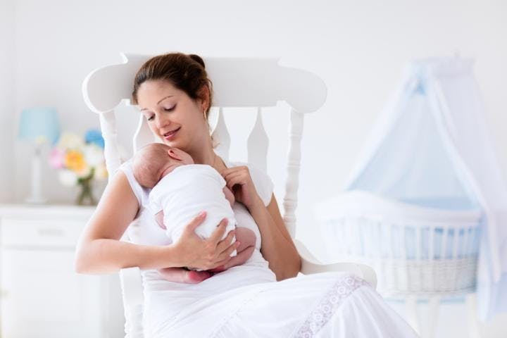 A young mother holding her baby as she is trying to breastfeed on a rocking chair