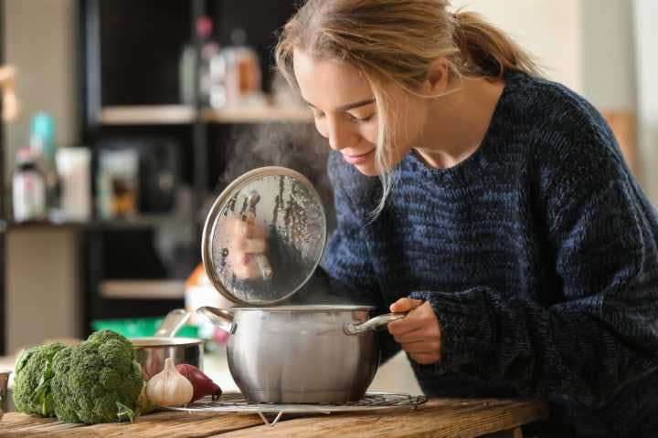A woman smelling herbal soup inside a pot to relieve her asthma symptoms