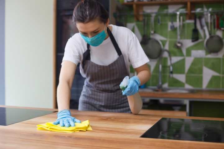 Woman in protective mask cleaning a table from dust