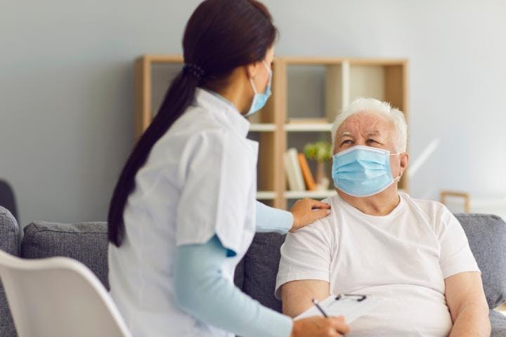 An old man wearing mask at home suffering from long covid, talking with a doctor