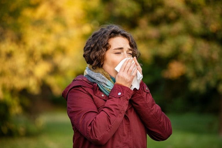 A woman sneezes on a tissue as she is experiencing flu symptoms outdoor