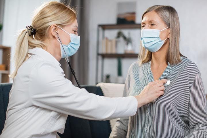 An older woman gets her breathing diagnosed by a female doctor wearing face masks