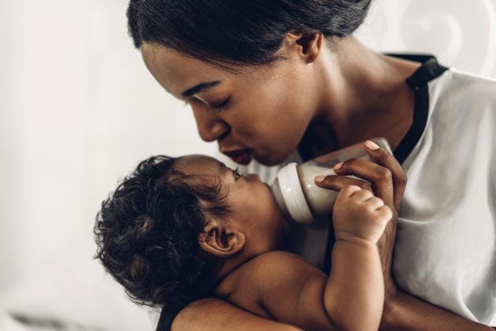 An african american woman bottle feeds her baby lovingly, white background