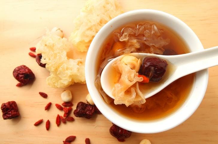 A bowl of white fungus soup with goji berries and red dates on a light wooden background.