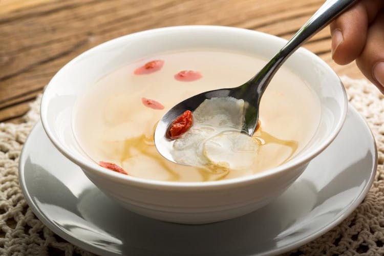 A herbal soup containing slices of American ginseng and goji berries inside a white ceramic bowl