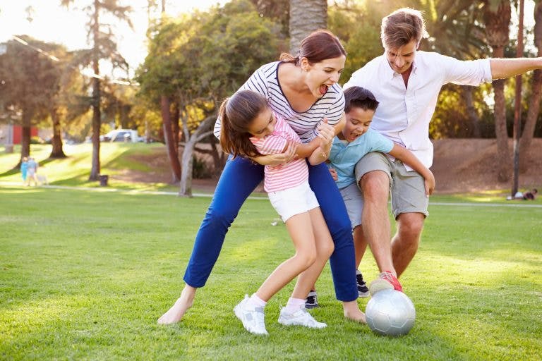 A happy and healthy family playing soccer in an outdoor park