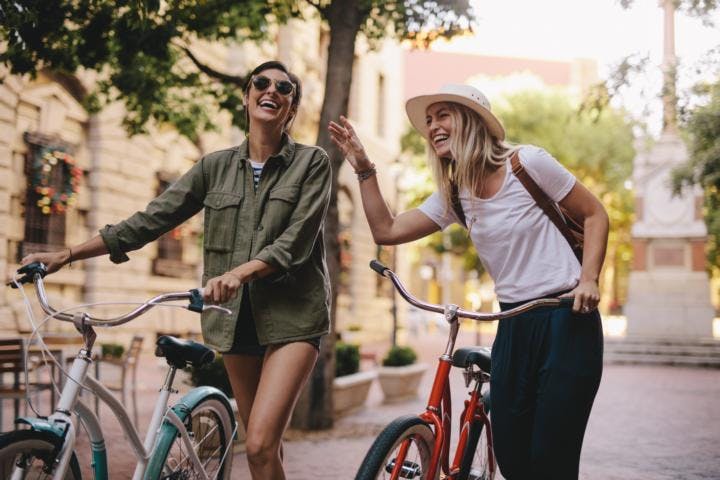 Two smiling young white women riding bicycles in the city