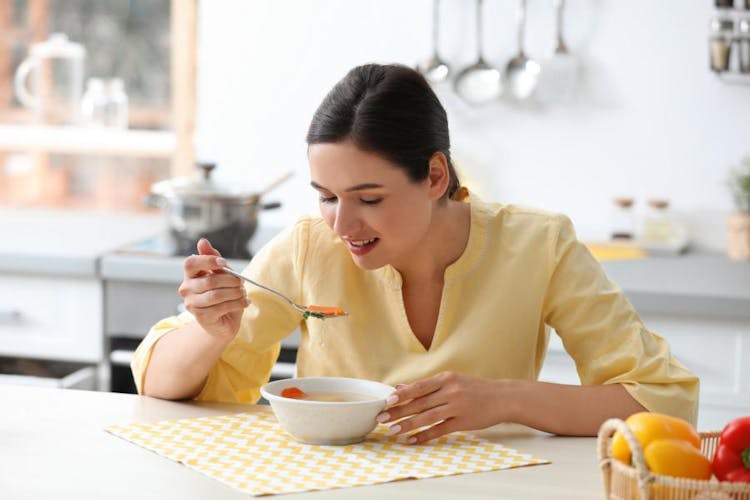 a woman on postpartum eating healthy soup with vegetables to nourish her body after giving birth