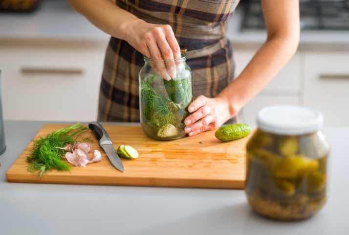 A woman putting slices of vegetables inside a jar to make fermented foods