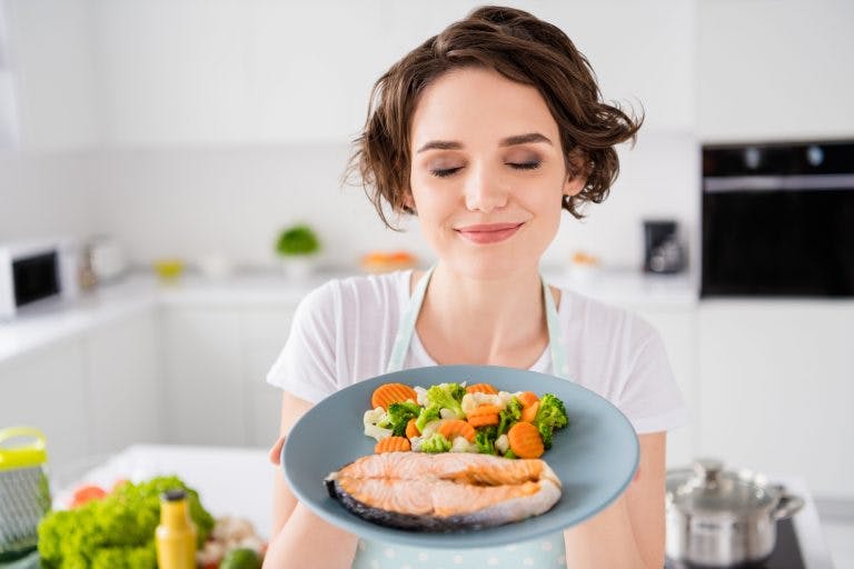 A young woman enjoying a plate of cooked salmon and steamed vegetables as a part of Mediterranean diet recipes
