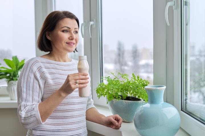 A woman looking out her window as she is drinking milk