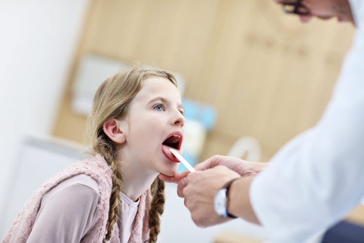 A girl with a sore throat sticking out her tongue for a doctor to diagnose her health condition