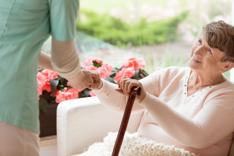 An elderly lady smiling at the caregiver, holding on to a walking cane