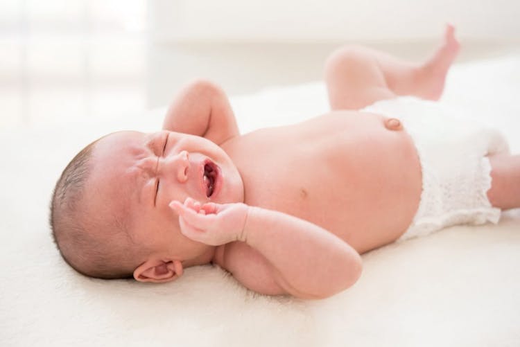 A crying baby wearing a diaper pictured on a white background