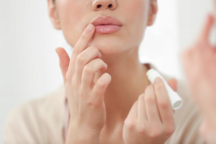 A young woman applying lip balm to her lips as a form of cold sore treatment 