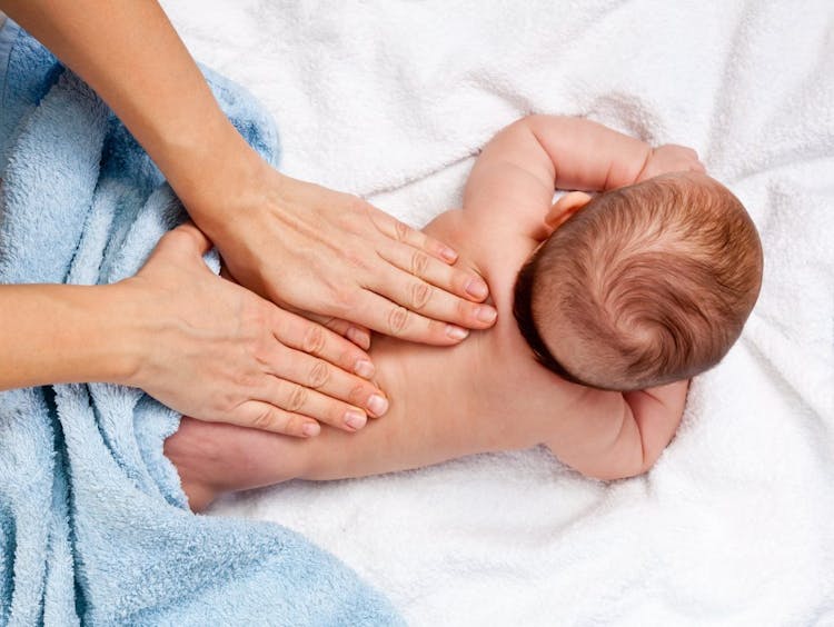 A pair of adult hands massaging the back of an infant, performing pediatric tuina