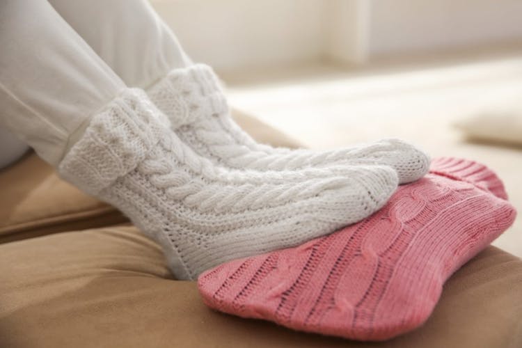 A woman keeping her feet warm by wearing wool socks and applying a heat pack to the bottom of her feet