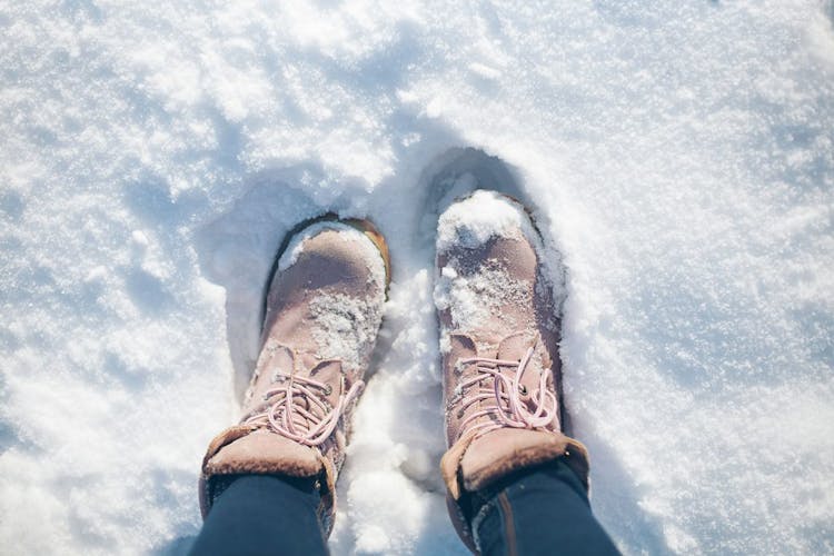 A close-up of a woman's pair of brown winter boots surrounded by snow