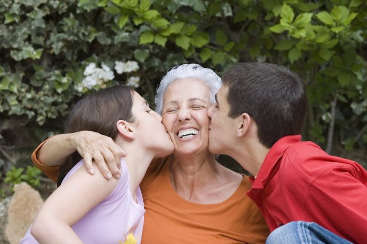 Two young children kissing their grandma on each cheek