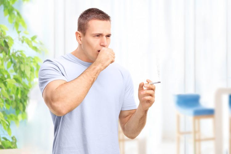 A young man holding a cigarette and experiencing smoker's cough