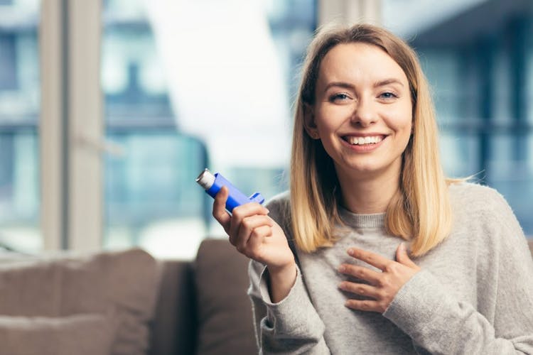 A smiling young woman holding an asthma inhaler 