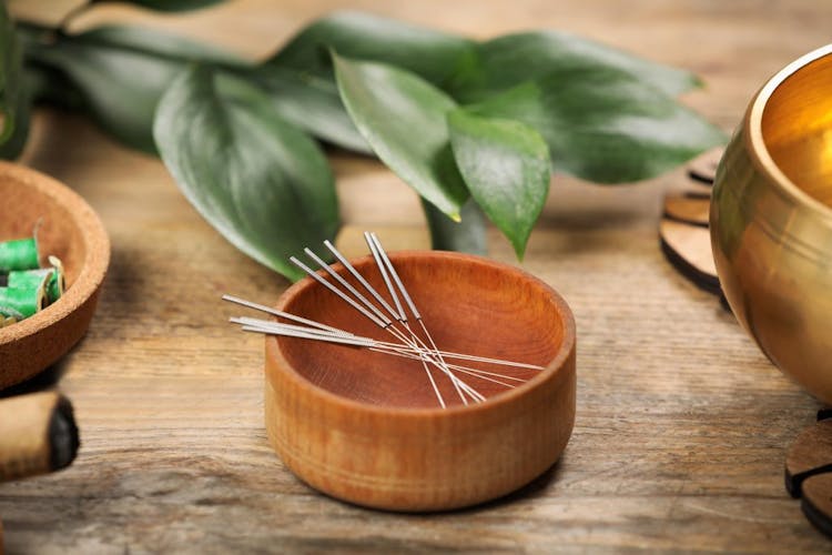 Acupuncture needles pictured in a wooden bowl on a wooden table 