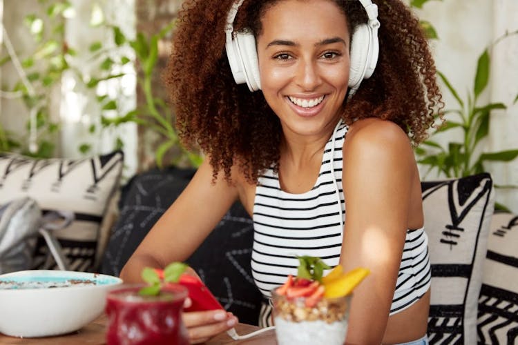 A smiling, confident young woman listening to music and eating healthy